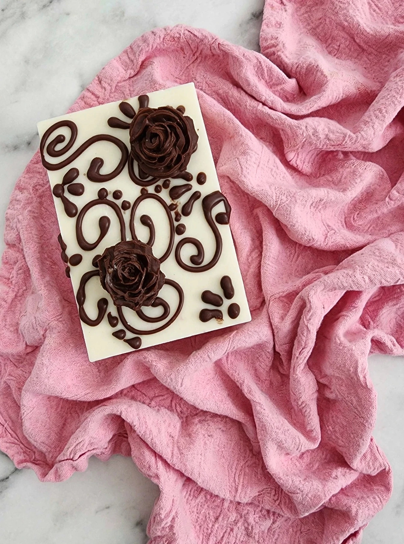 White chocolate Rice Krispy treat with dark chocolate rose and scroll designs on pink fabric