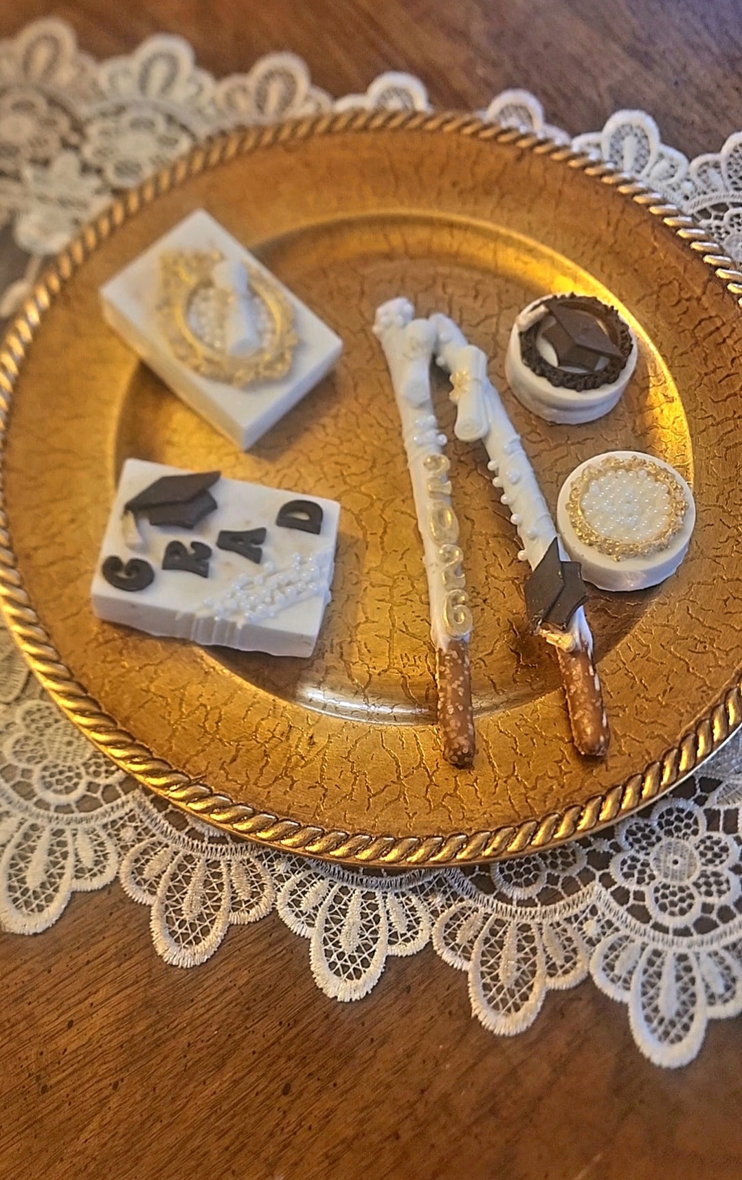 Graduation-themed white chocolate treats including GRAD Rice Krispy treats, pretzel rods, and decorated Oreos on a gold plate