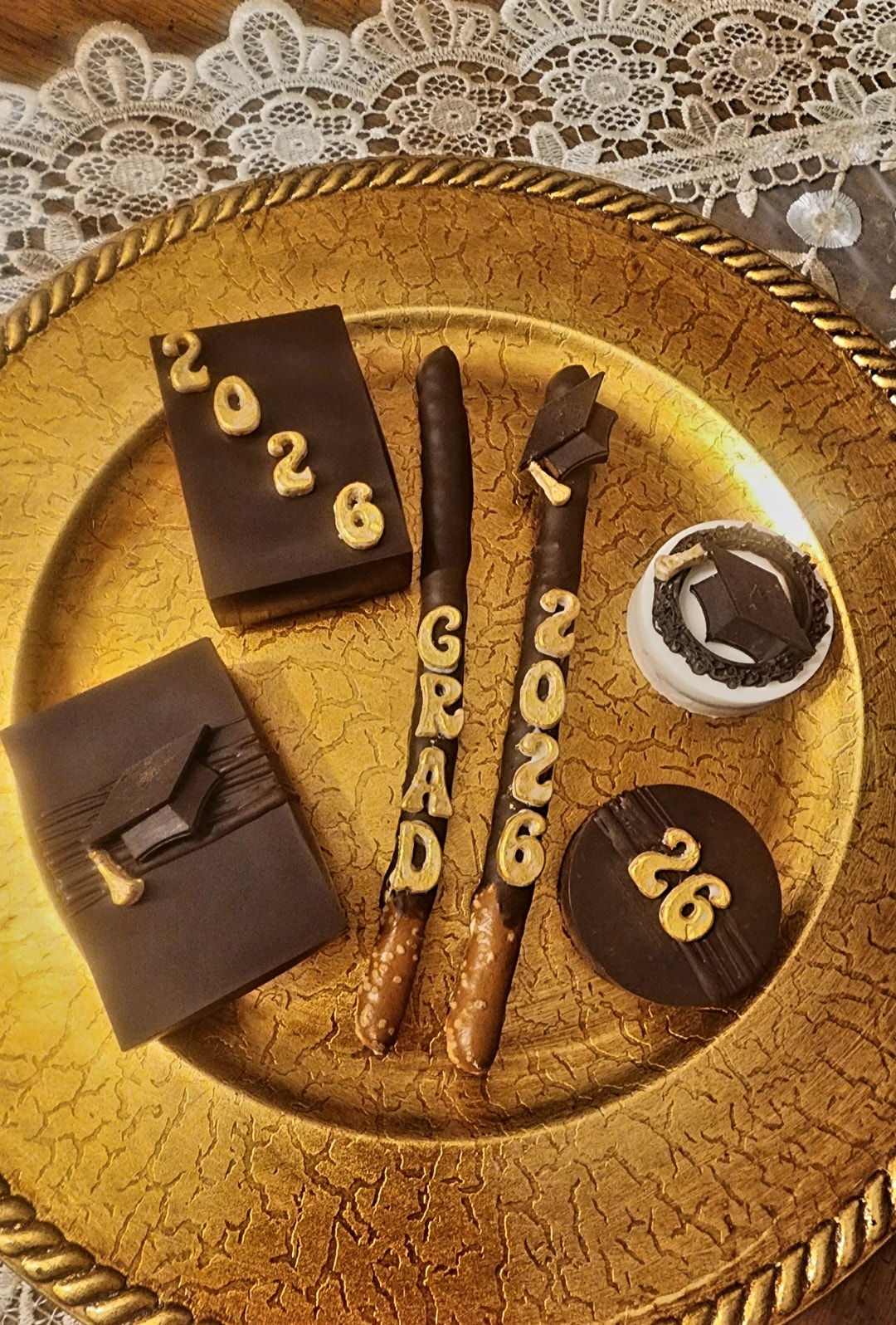 Dark chocolate graduation treats with gold 2026 lettering including diploma Rice Krispy treats and graduation cap Oreos