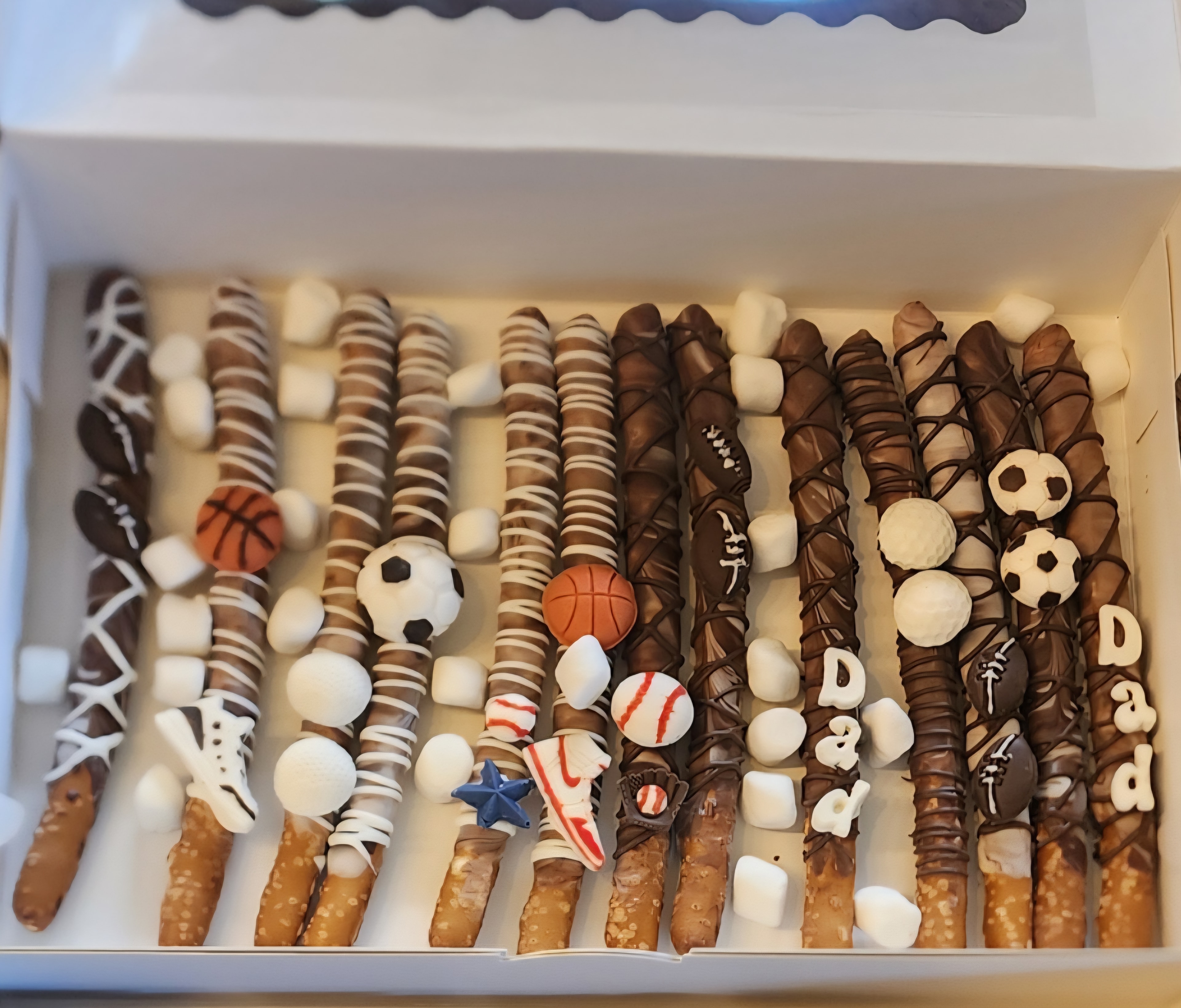 Chocolate-covered pretzel rods decorated with sports ball toppers in a gift box